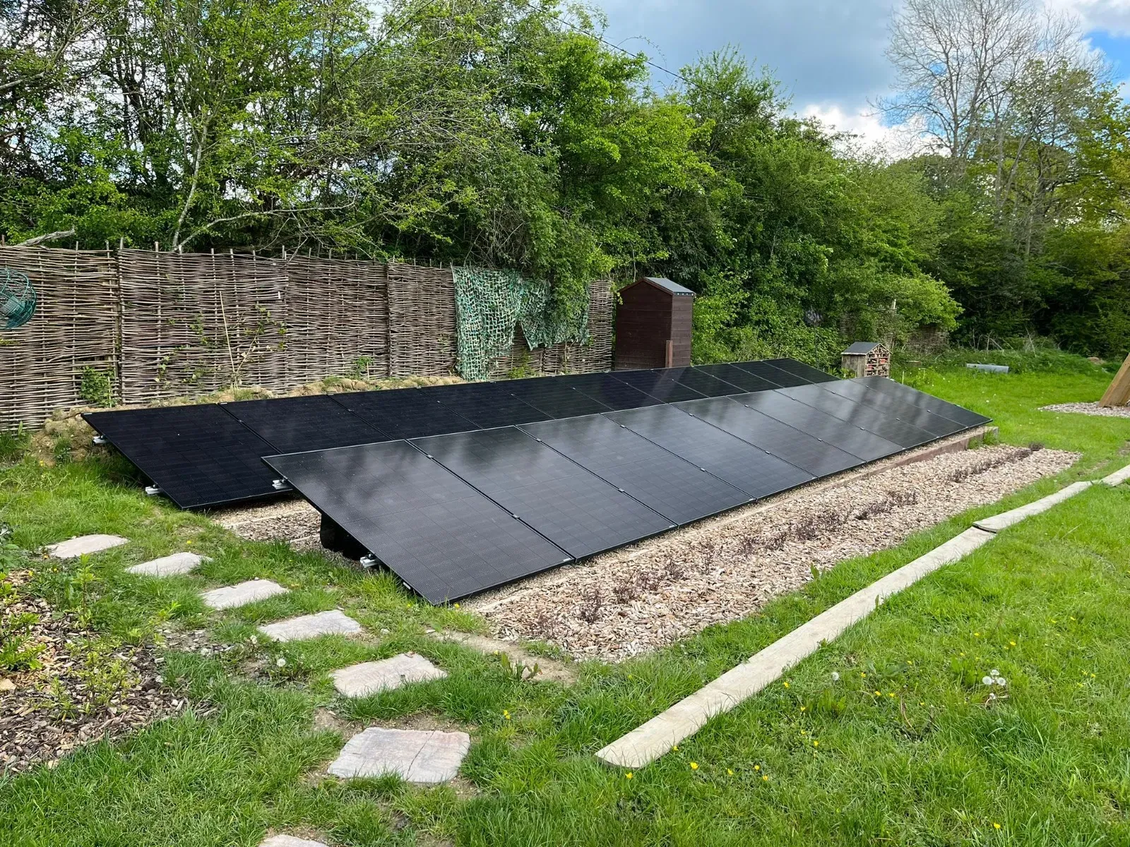 A ground-mounted solar array on a lawn beside a hedge