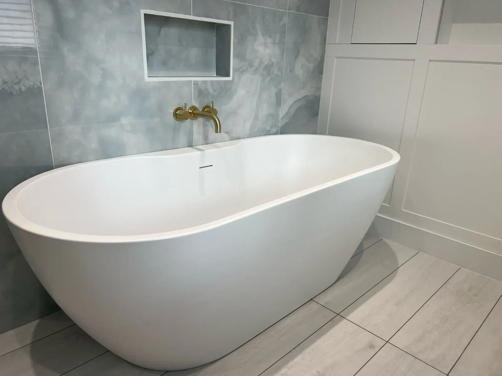 A freestanding bath in a panelled bathroom with marbled tiles