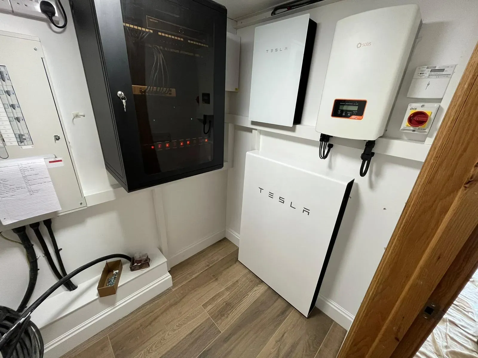 Tesla battery units installed in a utility room with a fridge alongside