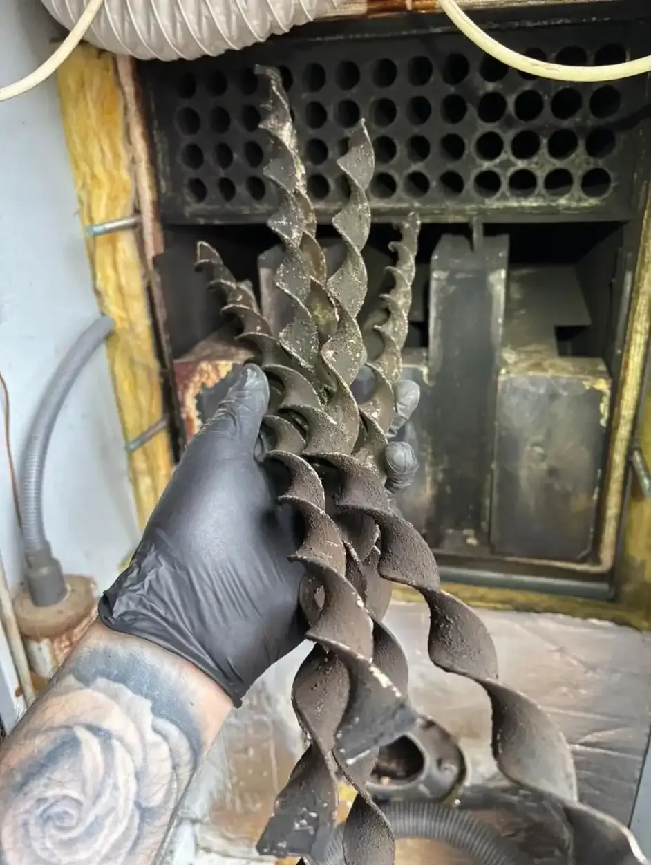 A Paynes engineer's gloved hand holding a cleaned boiler component beside the open casing